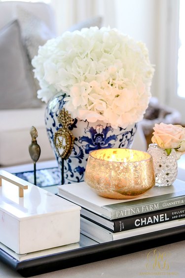 Close-up of coffee table vignette with white flowers in blue vase, candle, and decorative books