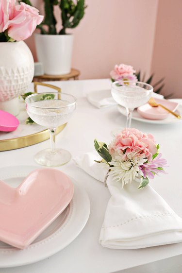 Soft-pink heart plates on a white tablecloth with floral napkin rings.
