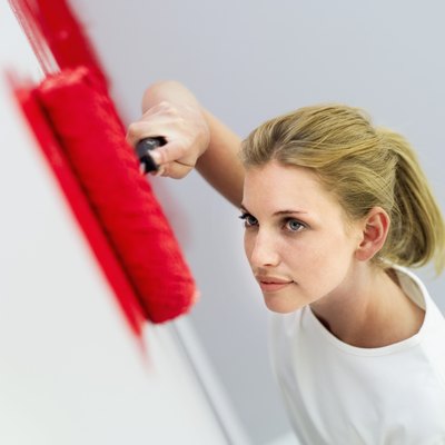 high angle view of a young woman painting a wall red with a paint roller