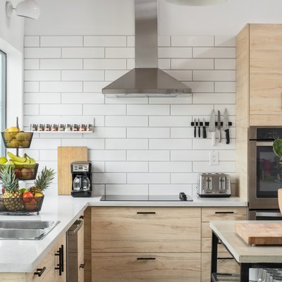 corner of kitchen with large windows, subway tile wall, pale wood cabinetry