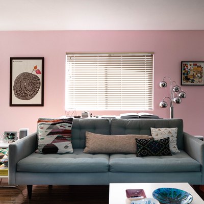 living room space with pink wall and blue couch and framed artworks on the wall