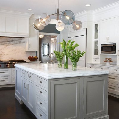 Kitchen with white cabinets, marble backsplash, kitchen island with gray cabinets. Modern glass chandelier.