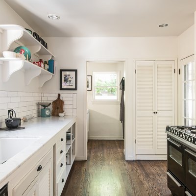 galley kitchen with white walls, white cabinetry, black stove