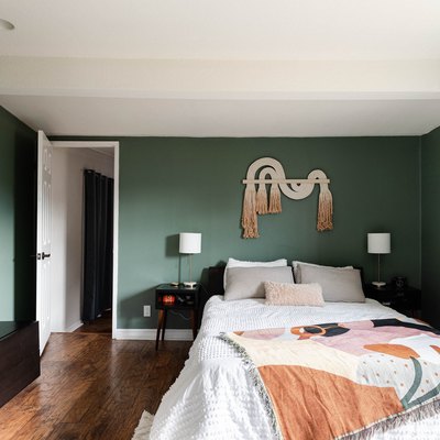 green bedroom with wood floors, white bed, artistic quilt