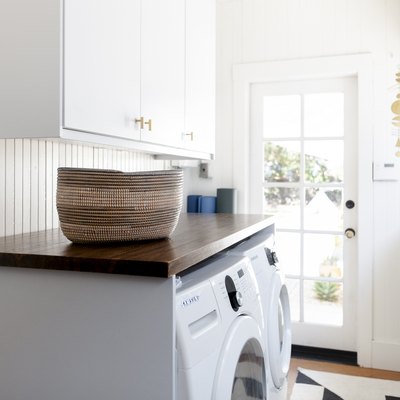 white laundry room idea with wood countertop over appliances and rug on the floor