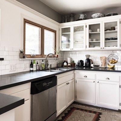 kitchen with white kitchen cabinets and glass inserts, dark countertops and subway tile backsplash