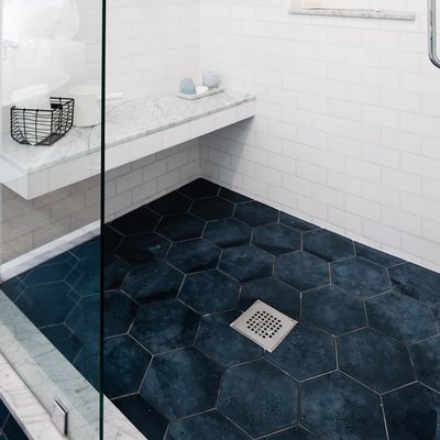 shower with blue hexagon floor tile, white subway wall tile, marble shower bench, glass doors, silver shower drain