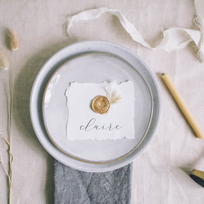 DIY gold wax seal place card with dried florals on top of place setting on table