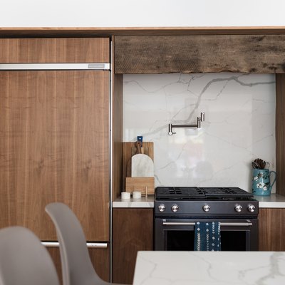 focus on stove with wood cabinet surround, marble backsplash, pot fillerf aucet