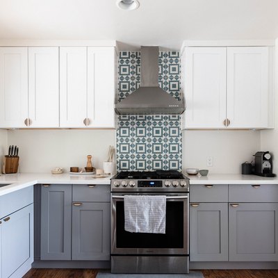 two-tone kitchen with gray lower cabinets, white uppers and tiled backsplash behind vent hood