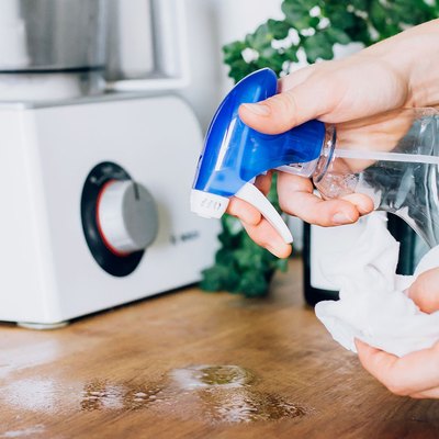 person spraying wood cutting board with cleaning product in spray bottle