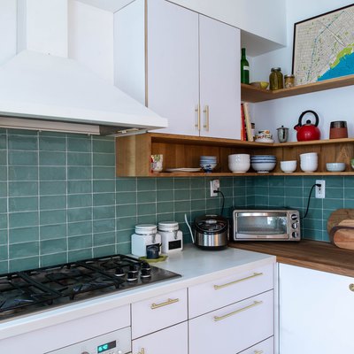 kitchen with blue tile backsplash, white cabitnets, white range hood and stove top