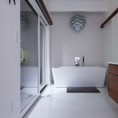 white freestanding tub, decorative hanging pendant above the bath, wood vanity, glass shower door