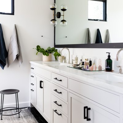 white bathroom vanity with black hardware, double sinks with silver faucet, three hanging towels, black stool, rectangular mirror with black trim