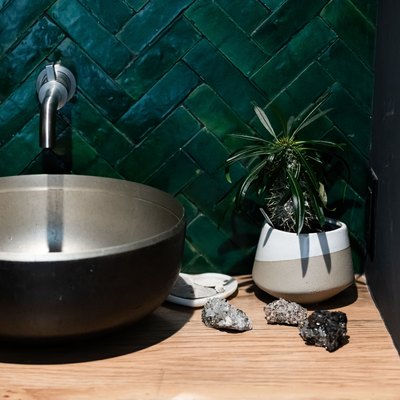 green herringbone tile backsplash, black vessel sink with silver wall-mounted faucet, wood bathroom vanity top, vase with succulent