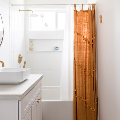 bathroom with brass fixutures, bowl sink, cicular mirror and rust-orange shower curtain