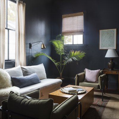 a sitting area with the walls painted a moody black, a white couch, green mid-century arm chairs, and a solid wood coffee table