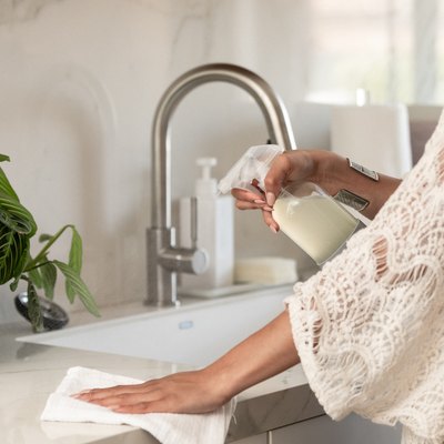 woman cleaning kitchen counter with spray and towel