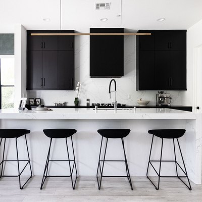 modern kitchen with white stone kitchen island, modern light fixture, black cabinets and black bar stools