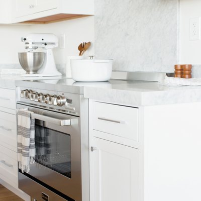 White kitchen cabinets with white marble backsplash, induction stove, mixer.