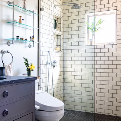 bathroom shower with white subway tile, blue bathroom vanity with sink, toilet and over-the-toilet storage
