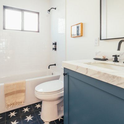 blue and stone bathroom vanity with sink, rectangular mirror with black trim, toilet, bathtub/shower combo and star-tiled floor