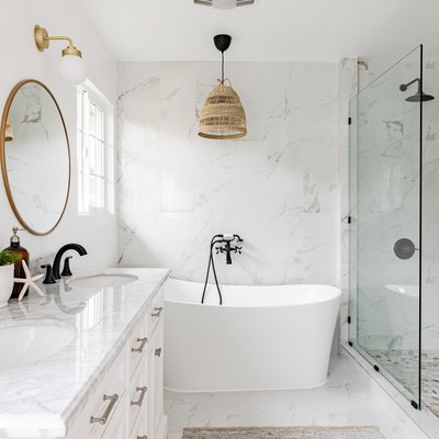 white bathroom, quartz countertop on white vanity, large white soaking tub, glass shower, two round mirrors with gold trim