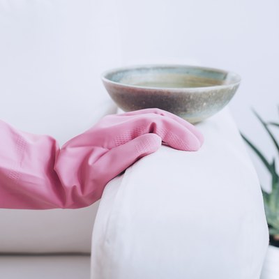 person wearing a pink rubber glove placing their hand on couch armrest with ceramic bowl