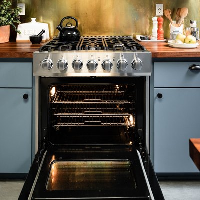 open stainless steel oven surrounded by light blue cabinets and wood countertops
