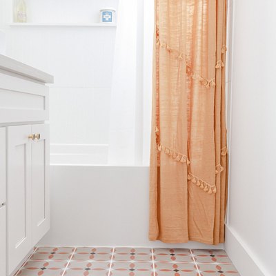 small bathroom with vinyl floor with orange, black and white pattern, white vanity, white bathtub, orange shower curtain