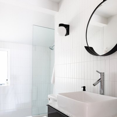 white vessel sink with silver faucet, round mirror with black trim, shower with glass door, white vertical rectangular tile