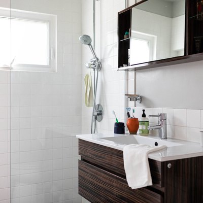 surface-mount wood medicine cabinet with mirror in the center, brown vanity with white ceramic top, white tile shower with glass door
