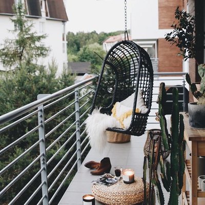 bohemian balcony idea with black hanging chair and woven floor pouf