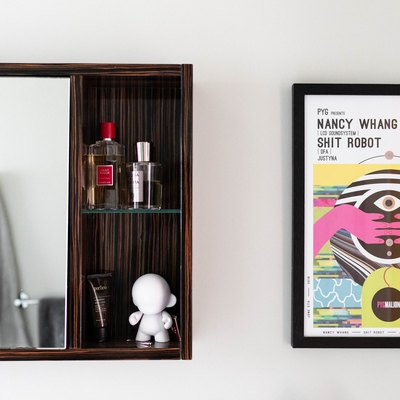 wood surface-mount medicine cabinet with beauty products inside, framed concert poster