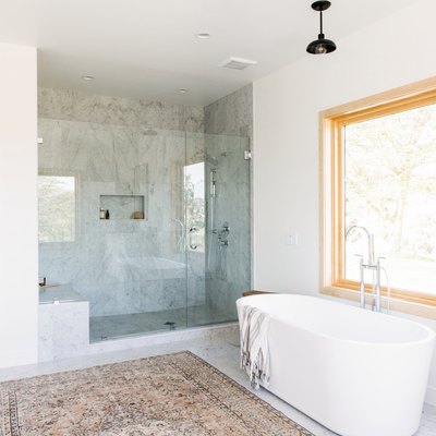 bathroom with freestanding white tub, walk-in shower with glass door, large window, multicolored area rug