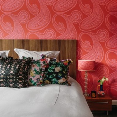 vermillion color wallpaper, wood headboard, floral throw pillows, navy blue door, lamp with red patterned lampshade.