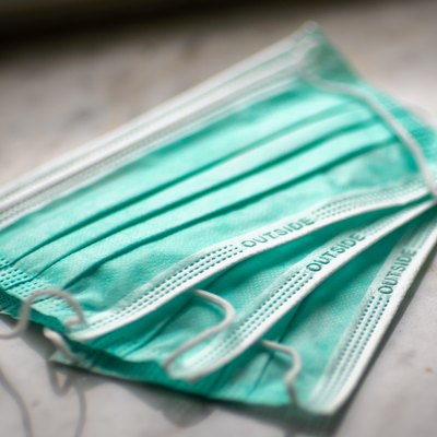 three green disposable face masks on a white marble countertop