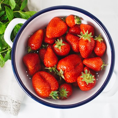 strawberries in ceramic bowl next to fresh green herbs