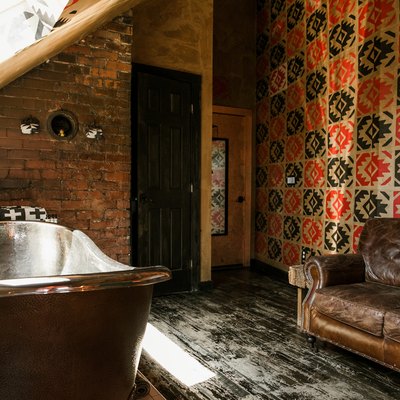freestanding copper bathtub, distressed black wood floors, exposed brick walls, patterned red and black walls, leather couch