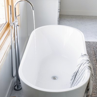 white freestanding tub with water flowing from floor-mount silver faucet, striped towel draped over the side, area rug, bathroom vanity with marble counters