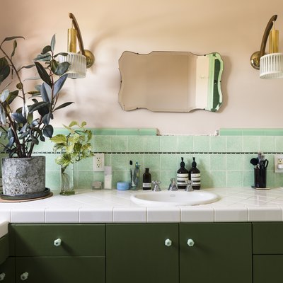 bathroom sink with green backsplash wall and small mirror