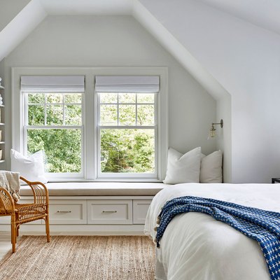 attic apartment with window seat, cane chair, white walls, white bedding, blue throw.