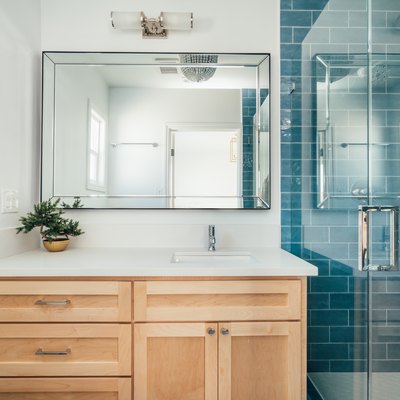 bathroom with teal subway shower tile, glass shower door, light wood bathroom vanity, rectangular mirror with overhead lighting