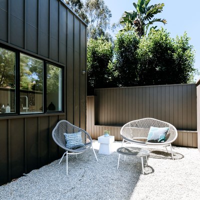 a side yard of a modern home with a pea gravel patio, white mid-century modern patio furniture