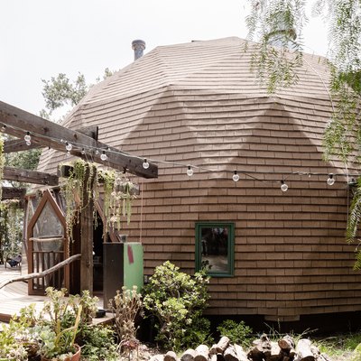 A brown dome-shaped home with a lush garden and string lights strung off the pergola