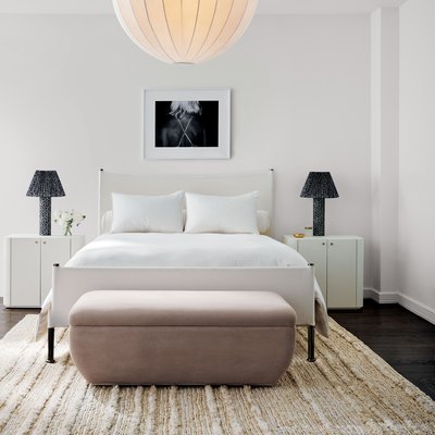 bedroom with white bedding, blush bench, and black table lamps