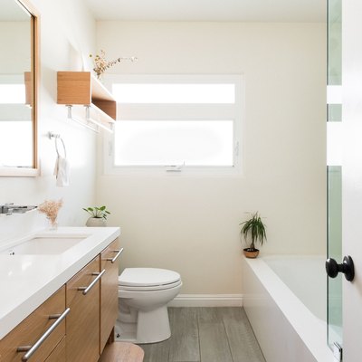 bathroom with white alcove bathtub, half glass shower door, white toilet, over-the-toilet wooden shelf, wood vanity with large silver drawer pulls