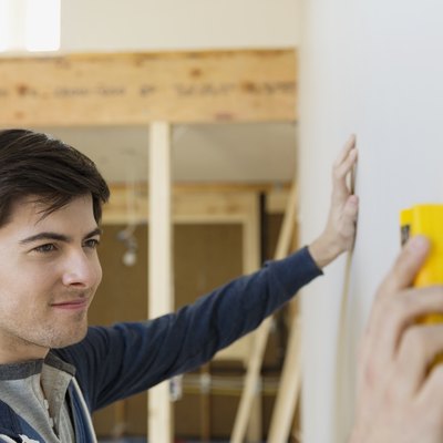 Young man with stud finder examining wall at home
