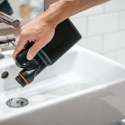 Removal of blockage in bathroom sink; the hand of a man pouring drain cleaner in a drain.