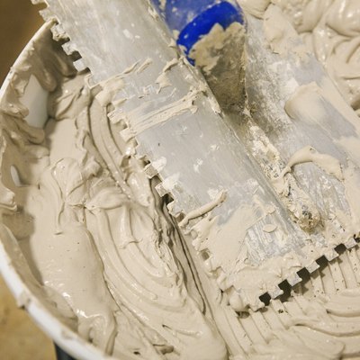 Close up of a tiling trowel and bucket of tile adhesive.